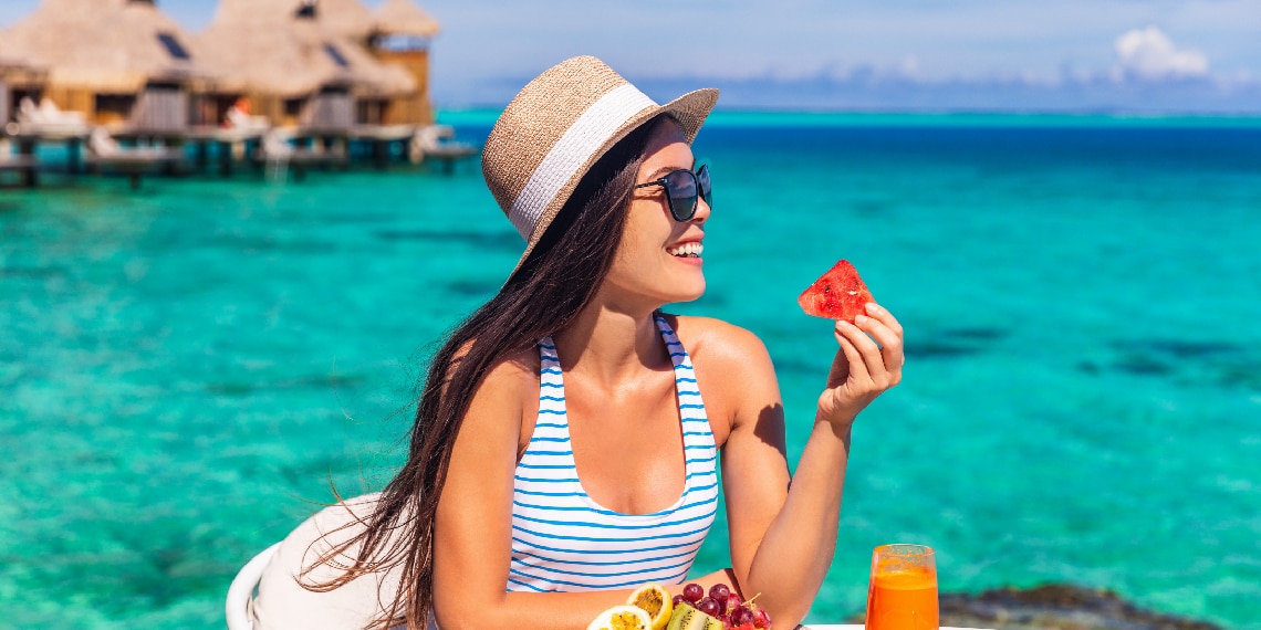 Photo of woman wearing glasses and eating a piece of fruit in a warm tropical location.