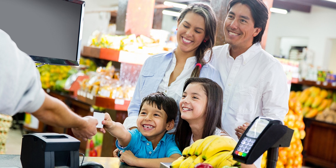 Photo of Hispanic family with young child handing credit card to store cashier.