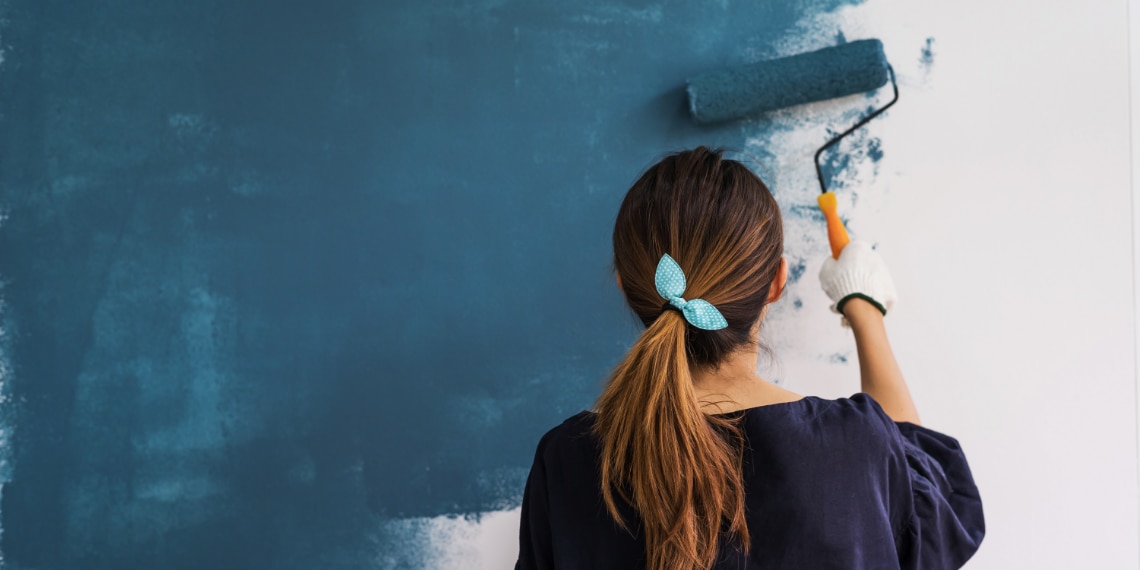 Photo of a young woman painting a wall inside a home.