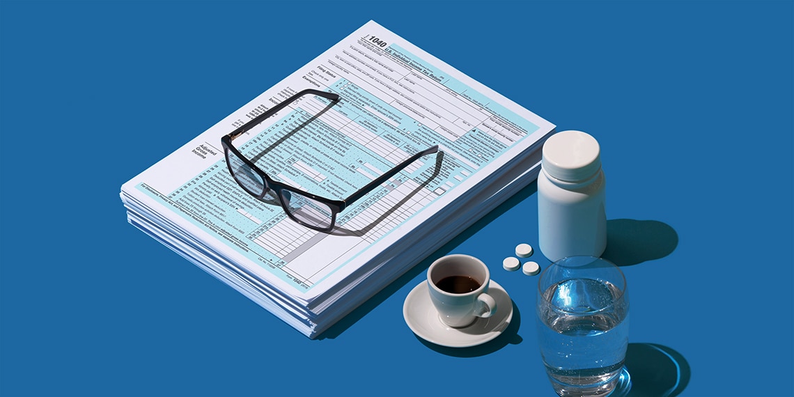 Tax forms with glasses, coffee, pills and water.