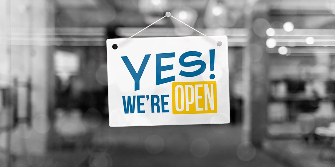 Sign in a store window saying 'yes we're open.'