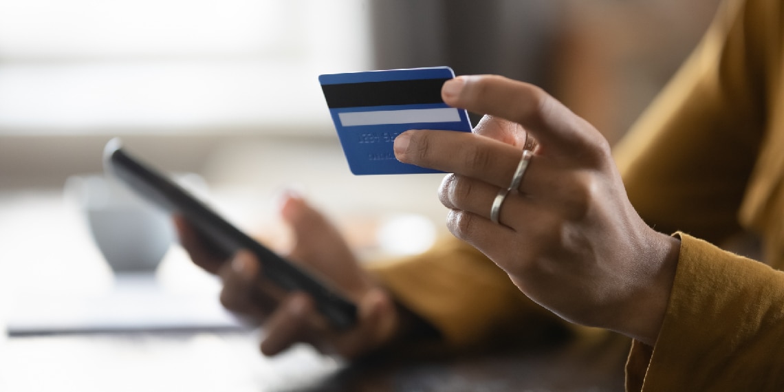 Photo of woman holding a credit card in one hand and smartphone in the other.